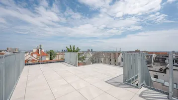 Geräumige Dachterrasse mit hellen Fliesen, Metallgeländer und weitem Blick über die Stadt.