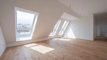 Heller Dachgeschossraum mit Holzboden und mehreren Dachfenstern, die viel Tageslicht hereinlassen.