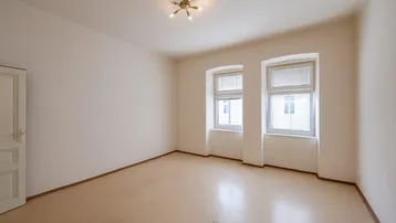 Helles, leeres Zimmer mit zwei Fenstern und schlichten weißen Wänden, bereit zur individuellen Gestaltung.