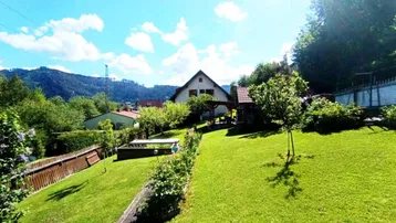 Weitläufiger Garten mit Rasenfläche, Bäumen und Blick auf die umliegende Hügellandschaft.