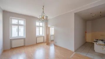 Heller Wohnraum mit Laminatboden und Fenstern, angrenzend an einen Küchenbereich.