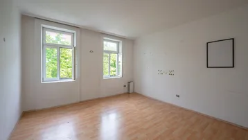 Helles, leeres Zimmer mit zwei Fenstern und Laminatboden, bereit zur individuellen Gestaltung.