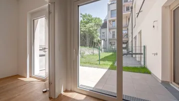 Heller Raum mit Holzboden und Zugang zu einer gefliesten Terrasse und einem kleinen Gartenbereich.