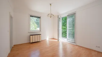 Helles Zimmer mit Parkettboden und Zugang zu einem Balkon, umgeben von Bäumen.