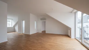 Helles, offenes Wohnzimmer mit Parkettboden, Dachschrägen und Zugang zum Balkon.