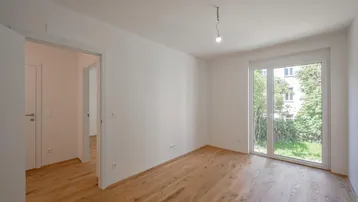 Heller Raum mit Holzboden und Zugang zum Garten, ideal als Wohn- oder Schlafzimmer.