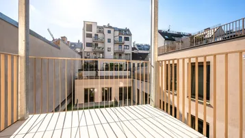 Blick von einem modernen Balkon mit Holzfliesen auf den Innenhof und umliegende Gebäude.