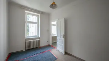 Leeres Zimmer mit Fenster, Heizkörper und Teppichboden, bereit für Renovierung.