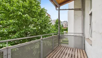 Gemütlicher Balkon mit Holzboden und Metallgeländer, umgeben von üppigem Grün und Bäumen.