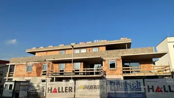 Rohbau eines modernen Wohngebäudes mit sichtbaren Ziegelwänden und Betonelementen unter klarem Himmel.