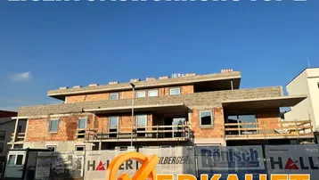 Neubau im Bau mit moderner Architektur und großen Fensteröffnungen unter klarem Himmel.