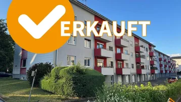 Mehrfamilienhaus mit mehreren Etagen, Balkonen und einer gepflegten Grünfläche im Vordergrund.