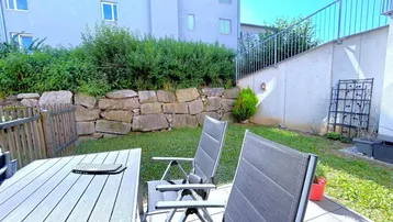 Gemütlicher Außenbereich mit Terrasse, Rasenfläche und Gartenmöbeln vor einem Wohngebäude.