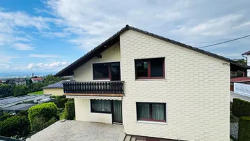 Zweistöckiges Einfamilienhaus mit Balkon und Blick auf die umliegende Landschaft unter blauem Himmel.