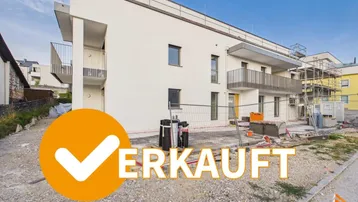 Modernes weißes Gebäude im Bau mit Balkonen und Flachdach, umgeben von einer Baustelle.