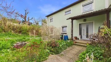 Eingangsbereich eines Hauses mit grün gestrichener Fassade und einem kleinen Vorgarten.
