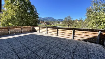 Große gepflasterte Terrasse mit Holzzaun und weitem Blick auf die Berge und Landschaft.