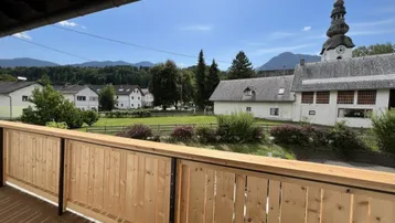 Geräumiger Balkon mit Holzboden und Geländer, bietet einen weiten Blick auf die umliegende Landschaft und Berge.