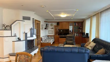 Geräumiges Wohnzimmer mit Kachelofen, Ledersofas und Holzmöbeln, bietet viel Platz zum Entspannen.