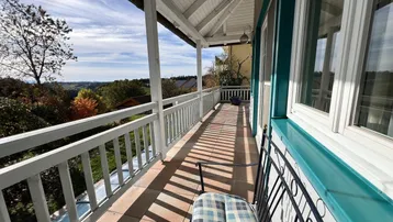 Langer Balkon mit Holzgeländer und weitem Blick über die hügelige Landschaft, sonnig und offen.