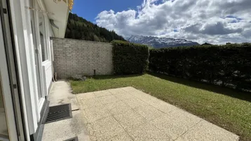 Gepflasterte Terrasse mit Rasenfläche und Blick auf die umliegenden Berge unter bewölktem Himmel.