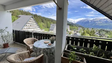 Möblierter Balkon mit Korbstühlen und einem Tisch, der einen weiten Blick auf die Berge und die umliegende Landschaft bietet.