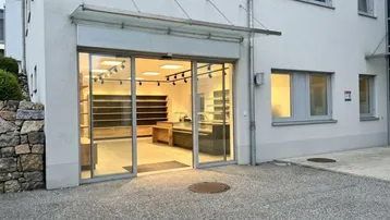 Modernes Geschäftsgebäude mit großer Glasfront und leerem Ladenlokal im Erdgeschoss.