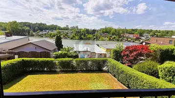 Blick aus dem Fenster auf einen gepflegten Garten mit Hecken und einem See im Hintergrund.