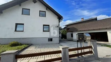 Außenansicht eines weißen Einfamilienhauses mit gepflasterter Auffahrt und Zaun unter blauem Himmel.