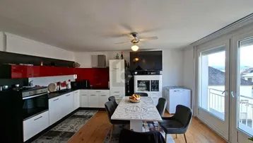 Moderne Küche mit roten Akzenten, Essbereich und Zugang zu einem Balkon, ausgestattet mit Holzfußboden.