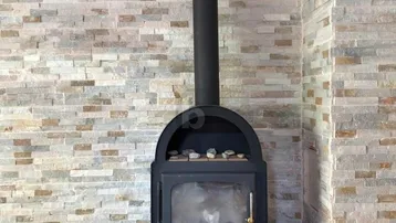 Moderner Kaminofen vor einer Wand mit Steinverkleidung und Fliesenboden.