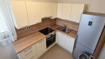 Moderne Einbauküche mit hellen Schränken, Holzarbeitsplatte und integrierten Geräten, inklusive Kühlschrank.