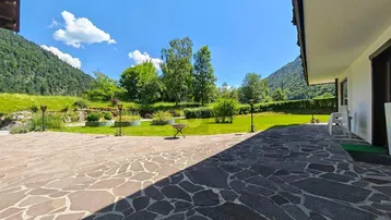 Große gepflasterte Terrasse mit angrenzendem Rasen und weitem Blick auf die umliegenden Berge.
