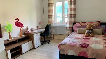 Helles Schlafzimmer mit Einzelbett, Schreibtisch und Stauraum, dekoriert mit bunten Elementen und Blick nach draußen.