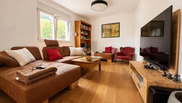 Helles Wohnzimmer mit bequemer Ledercouch, Holzboden und Blick ins Grüne.