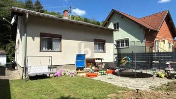 Gartenbereich hinter dem Haus mit Rasenfläche, Trampolin und Kinderspielgeräten unter blauem Himmel.