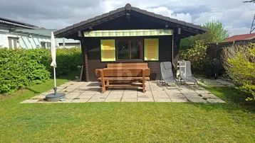 Kleines Holzhaus mit Terrasse, Gartenmöbeln und Rasenfläche, ideal für entspannte Stunden im Freien.