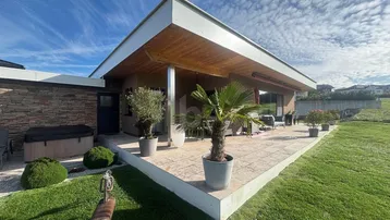 Moderne Villa mit großer gepflasterter Terrasse, Outdoor-Möbeln und Whirlpool im Gartenbereich.