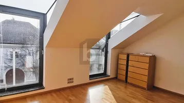 Heller Dachgeschossraum mit schrägen Wänden, Holzboden und großen Fenstern für viel Tageslicht.