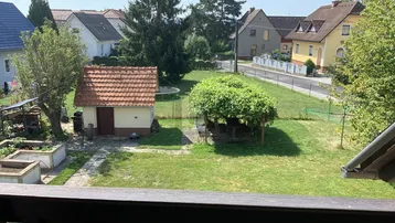 Großer Garten mit Rasenfläche, Gartenhaus und überdachtem Sitzbereich, umgeben von Wohnhäusern.