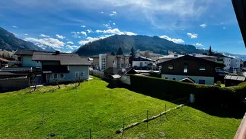 Weitblick über grüne Gärten und Dächer mit majestätischer Berglandschaft im Hintergrund.