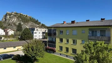 Gebäudeansicht mit grüner Umgebung und Blick auf eine historische Burg auf dem Berg.