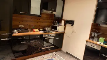 Moderne Küche mit schwarzen Hochglanzschränken, Holzarbeitsplatte und Teppich.