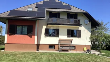 Hausfassade mit Photovoltaikanlage auf dem Dach, Balkon und kleinem Schaukelstuhl im Vorgarten.