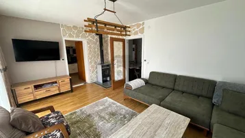 Helles Wohnzimmer mit Holzboden, modernem Kaminofen und gemütlicher Sitzecke.
