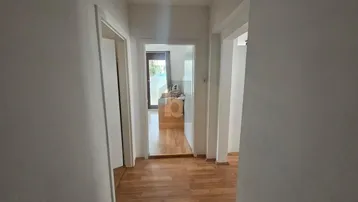 Heller Flur mit Holzboden und Türen zu verschiedenen Räumen, ein Spiegel reflektiert den Ausgangsbereich.