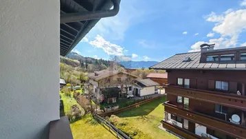 Blick von einem Balkon auf die umliegende Wohngegend mit grünen Hügeln und Bergen im Hintergrund.