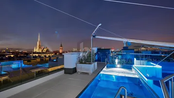 Dachterrasse mit beleuchtetem Pool und Panoramablick auf die Stadt bei Nacht.
