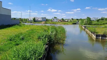 Blick auf das Gewässer mit modernen Gebäuden und grüner Uferlandschaft unter blauem Himmel.