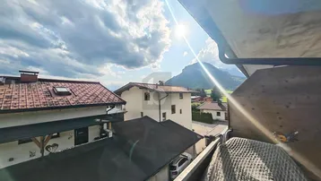 Sonniger Ausblick vom Balkon auf umliegende Häuser und die majestätische Berglandschaft.